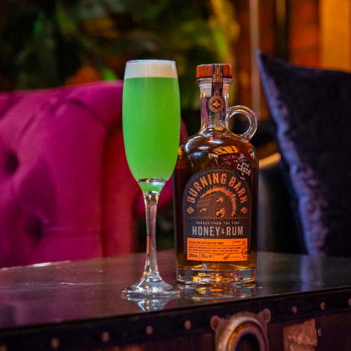 Yellow coloured cocktail in tall, thin cocktail glass with bar in background 