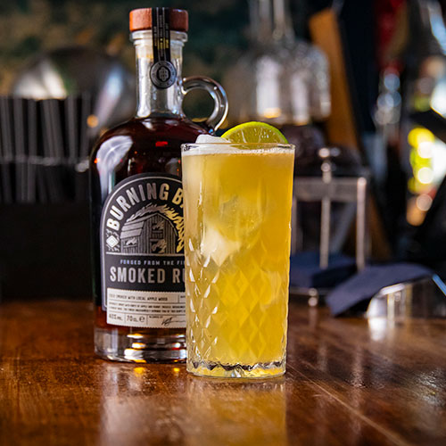 Dark N' Smoky cocktail with fresh lime slice, with cocktail bottle 