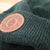 Close-up view of green beanie with Burning Barn logo on it